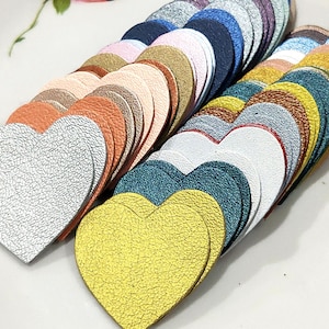 May include: A collection of leather heart shapes in various colours, including silver, gold, teal, white, and copper. The hearts are arranged in a fan shape, with the silver heart in the foreground.