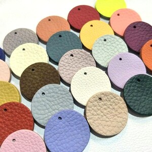 Könnte beinhalten: Sortiment von 20 runden Lederstücken in verschiedenen Farben, darunter Rosa, Blau, Grün, Braun, Gelb und Beige. Jedes Stück hat ein kleines Loch in der Mitte.