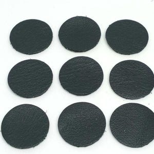 May include: Nine dark green leather circles, each approximately 5 cm in diameter, are arranged in three rows of three on a white surface.