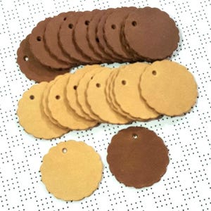 Op de afbeelding: Een stapel ronde papieren etiketten in bruin en beige met gegolfde randen en een geperforeerd gat bovenaan.