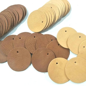 May include: A collection of round leather craft tags in two colours: brown and tan. The tags have a hole punched in the centre for attaching to items.
