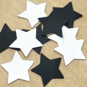 Op de afbeelding: Een verzameling zwarte en witte papieren sterren. De sterren zijn verspreid over een bruin, getextureerd oppervlak.