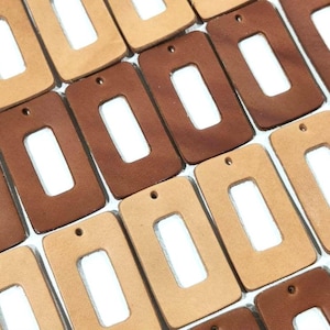 May include: A collection of rectangular leather craft blanks with a cut-out rectangle in the centre. The blanks are in two colours: brown and beige.