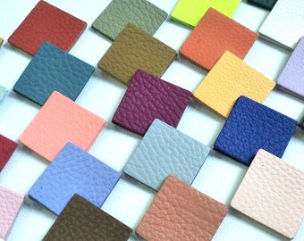May include: A collection of small, square leather samples in various colors, including pink, blue, green, brown, and purple. The samples are arranged in a diagonal pattern on a white surface.