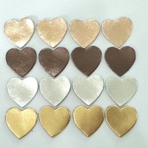 May include: A set of 18 heart-shaped leather patches in various metallic colors, including gold, silver, bronze, and copper. The patches are arranged in three rows of six, with each row featuring a different color.