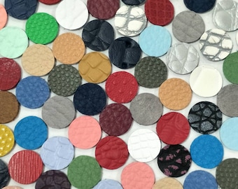 May include: Assortment of small, round leather pieces in various colors and textures. The leather pieces are arranged in a random pattern on a white surface.