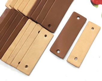 May include: A set of leather craft supplies, including two rectangular leather pieces with holes, one brown and one beige. The leather pieces are stacked on top of each other.