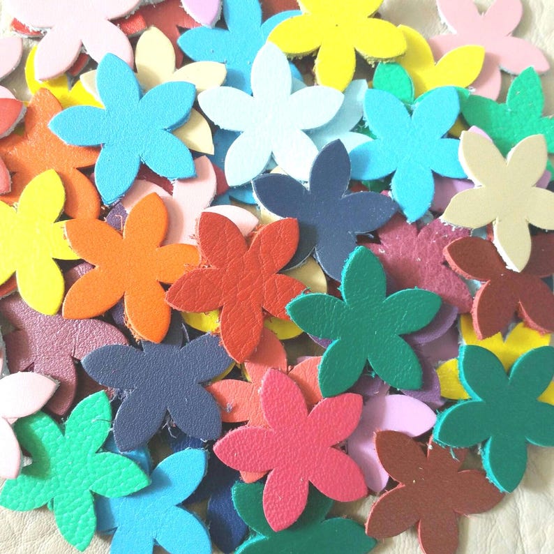 Op de afbeelding: Een verzameling van kleurrijke lederen bloemenvormen in verschillende kleuren, waaronder rood, oranje, geel, groen, blauw, paars, roze en bruin.