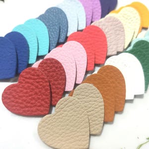 Könnte beinhalten: Sortiment aus Kunstleder-Herzformen in verschiedenen Farben, darunter Rot, Blau, Grün, Rosa, Weiß und Braun. Die Herzen sind in einem Halbkreis angeordnet.