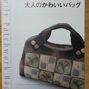 May include: A book cover showing a patchwork bag with a brown handle and decorative buttons. The bag is made of various fabric squares in shades of brown, green, and beige. Text on the cover reads "Daily Patchwork Bag" and Japanese text.