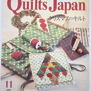 以下が含まれることがあります： 「Quilts Japan」の表紙は、クリスマスのキルトプロジェクトを紹介しています。緑と白のドット柄のキルトポーチ、クリスマスツリーのキルト、その他のキルト用品が含まれています。雑誌のタイトルは大きな赤い文字で書かれています。