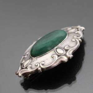 May include: A silver brooch with an oval-shaped green malachite stone set in a detailed, ornate design.
