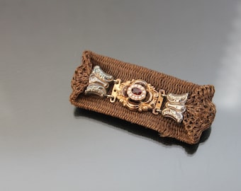 May include: A gold and silver hair comb with a red gemstone and pearl accents. The comb is on a brown fabric background.