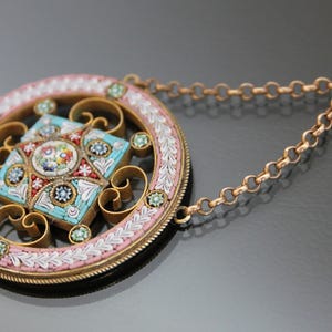 May include: A round pendant necklace with a detailed mosaic design in shades of blue, pink, and white. The pendant is surrounded by a delicate gold-colored frame and hangs from a gold-colored chain.
