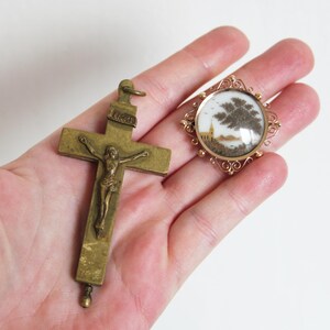 May include: A gold-toned crucifix pendant with a detailed figure of Jesus Christ.  Next to it is a round, gold-toned locket with a glass cover and a small, detailed, hair-art scene inside.