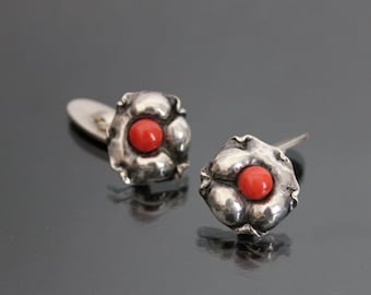 Puede incluir: Un par de gemelos de plata con una piedra de coral rojo en el centro de cada gemelo. Los gemelos tienen forma de flor.