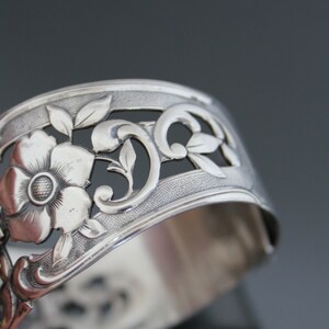 May include: Silver napkin ring with an ornate floral design. The ring is made of silver and has a delicate floral pattern.
