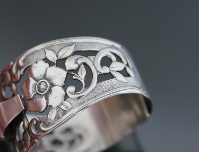 May include: Silver napkin ring with an ornate floral design. The ring is made of silver and has a delicate floral pattern.