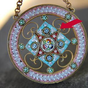 May include: A round pendant with a gold filigree design and a colorful mosaic center. The mosaic is made of small, colorful tiles in a geometric pattern. The pendant is suspended from a gold chain.