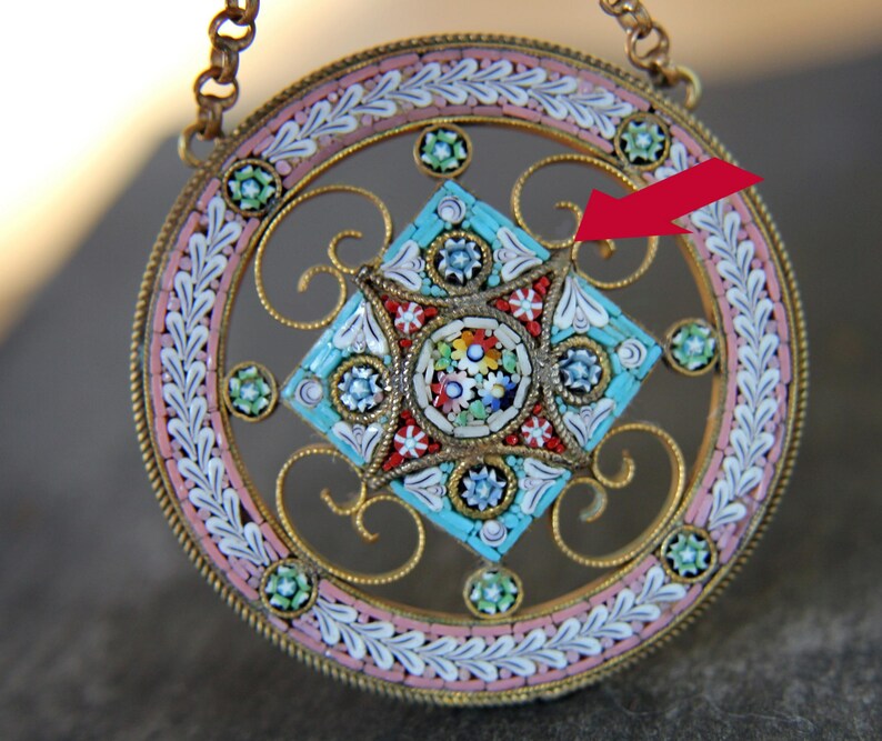 May include: A round pendant with a gold filigree design and a colorful mosaic center. The mosaic is made of small, colorful tiles in a geometric pattern. The pendant is suspended from a gold chain.
