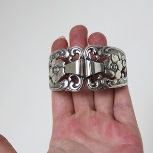 May include: Silver napkin ring with a floral design. The ring is open and has a hinge.