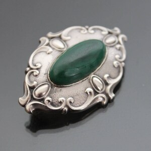 May include: A silver brooch with an oval green stone set in a decorative filigree design.