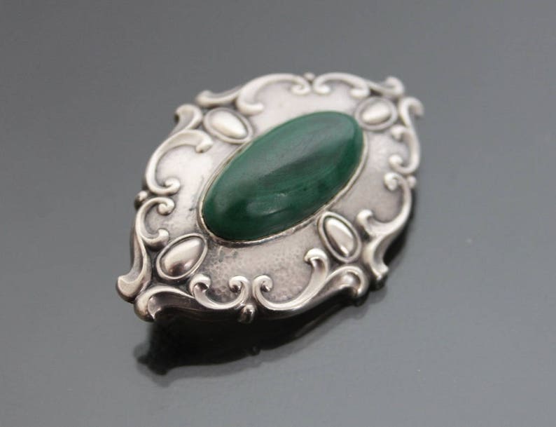 May include: A silver brooch with an oval green stone set in a decorative filigree design.