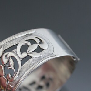 May include: Silver bracelet with an intricate floral design. The bracelet is made of silver and has a delicate, openwork design.