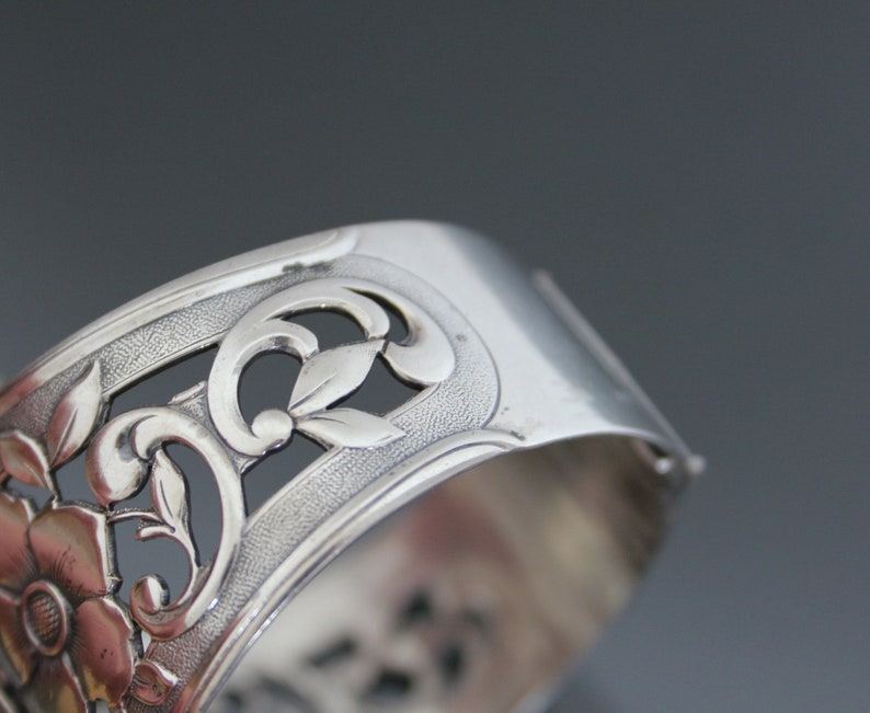 May include: Silver bracelet with an intricate floral design. The bracelet is made of silver and has a delicate, openwork design.