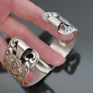 May include: Silver bracelet with an ornate floral design. The bracelet is open and has a hinged clasp.