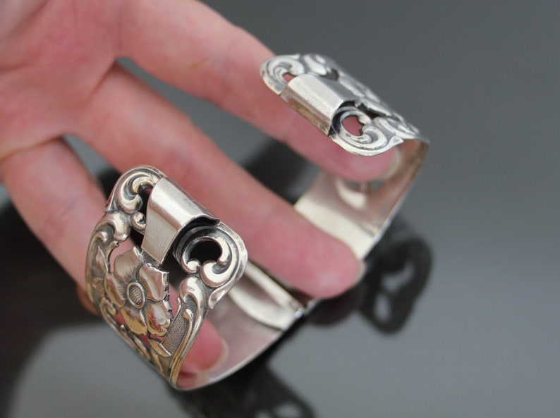 May include: Silver bracelet with an ornate floral design. The bracelet is open and has a hinged clasp.