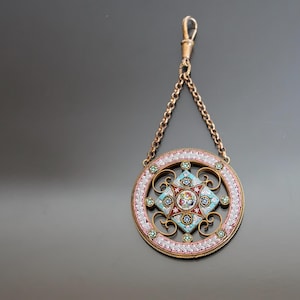 May include: A circular pendant with a delicate floral design in shades of pink, blue, and white. The pendant is made of micro mosaic and is attached to a gold chain.