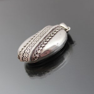 K&ouml;nnte beinhalten: Ein silbernes Medaillon mit einem komplizierten Design am Rand. Das Medaillon ist oval geformt und hat eine glatte Oberfl&auml;che.
