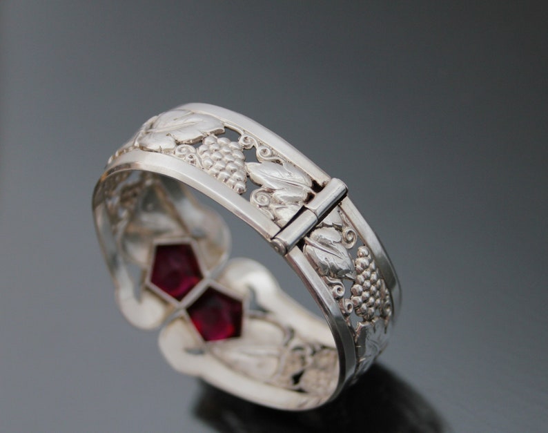 Puede incluir: Pulsera de plata con dise&ntilde;o de vid y dos piedras preciosas rojas. La pulsera tiene un cierre de bisagra.
