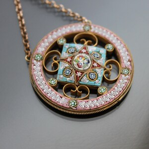 May include: A round pendant necklace with a delicate gold chain. The pendant features a square mosaic design with a star in the center. The mosaic is made of small, colorful tiles in shades of blue, green, pink, and red.
