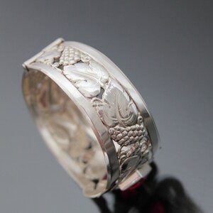 Puede incluir: Pulsera de plata con dise&ntilde;o de vid. La pulsera est&aacute; abierta y tiene una piedra roja en el cierre.