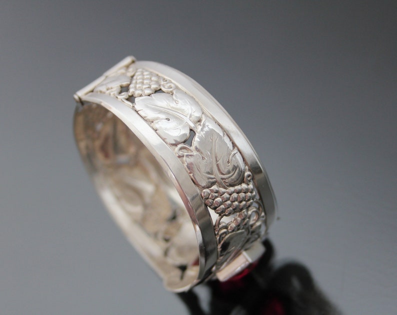Puede incluir: Pulsera de plata con dise&ntilde;o de vid. La pulsera est&aacute; abierta y tiene una piedra roja en el cierre.