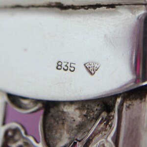 Puede incluir: Primer plano de un objeto plateado con el n&uacute;mero "835" y una marca en forma de diamante con las letras "RMW" en su interior.