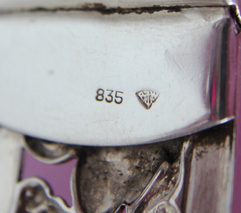 Puede incluir: Primer plano de un objeto plateado con el n&uacute;mero "835" y una marca en forma de diamante con las letras "RMW" en su interior.