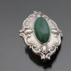 May include: A silver brooch with an oval-shaped green malachite stone set in a detailed, ornate design.