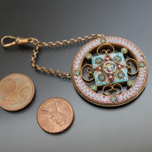 May include: A gold chain with a round pendant featuring a colorful mosaic design. The pendant is surrounded by a white and pink border with green accents.