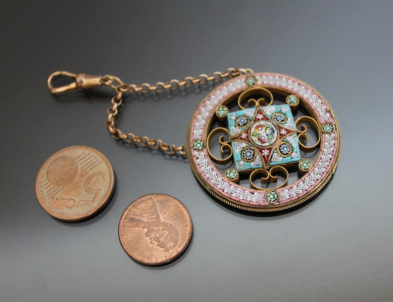 May include: A gold chain with a round pendant featuring a colorful mosaic design. The pendant is surrounded by a white and pink border with green accents.