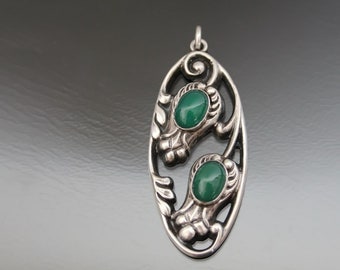 May include: A silver pendant with an oval shape and intricate floral design. Two green gemstones are set within the design.
