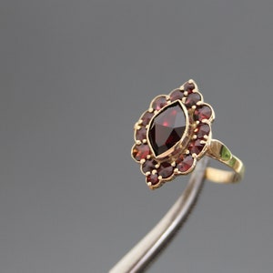 Può includere: Un anello d'oro con un grande granato rosso a forma di marquise circondato da granati rossi più piccoli.