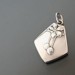 May include: A silver pendant with a floral design and two cherries. The pendant is in the shape of a diamond and has a smooth, polished finish.