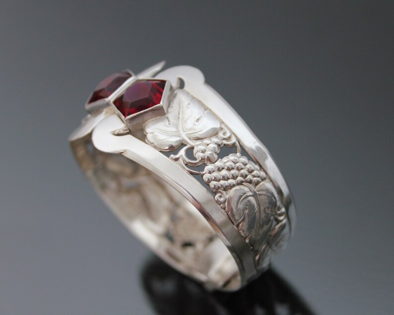 Puede incluir: Pulsera de plata con dise&ntilde;o de vid y dos piedras preciosas rojas.