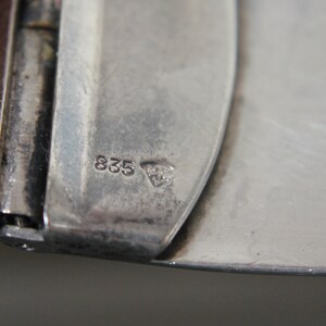 May include: Close-up of a silver metal object with the number "835" and a small triangle symbol stamped on it.