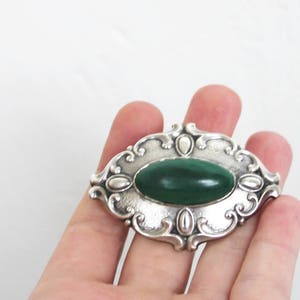 May include: A silver brooch with an oval green stone set in a decorative frame.