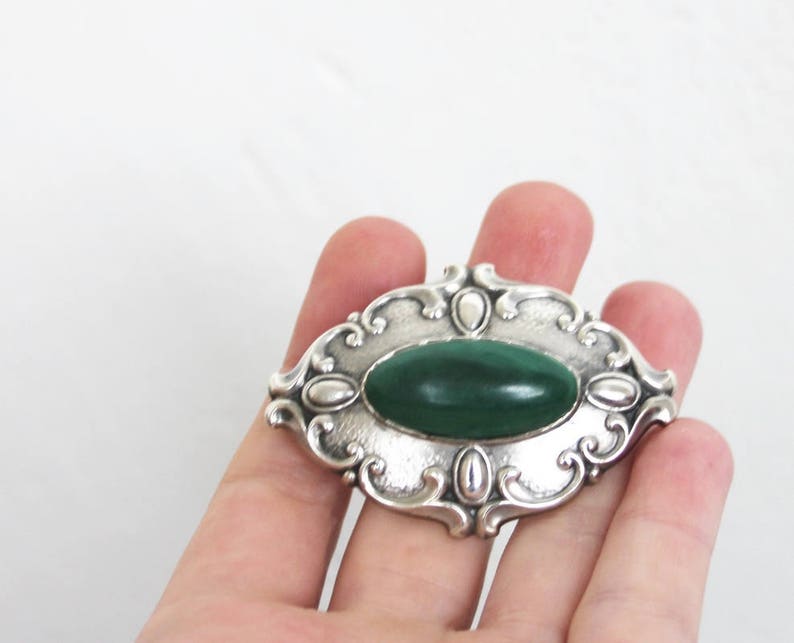 May include: A silver brooch with an oval green stone set in a decorative frame.