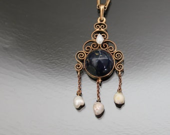 Puede incluir: Un collar de oro con un colgante de filigrana que tiene una piedra preciosa azul y tres perlas blancas colgando de la parte inferior.
